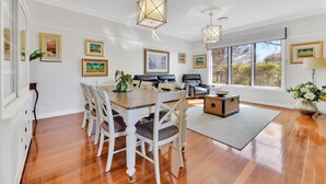 A dining area with a wooden table and chairs, a sofa, and a window with a view of trees.
