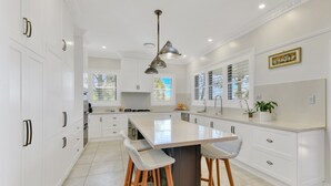 A modern kitchen with white cabinetry, a large island with bar stools, pendant lighting, and a view of the outdoors through windows.
