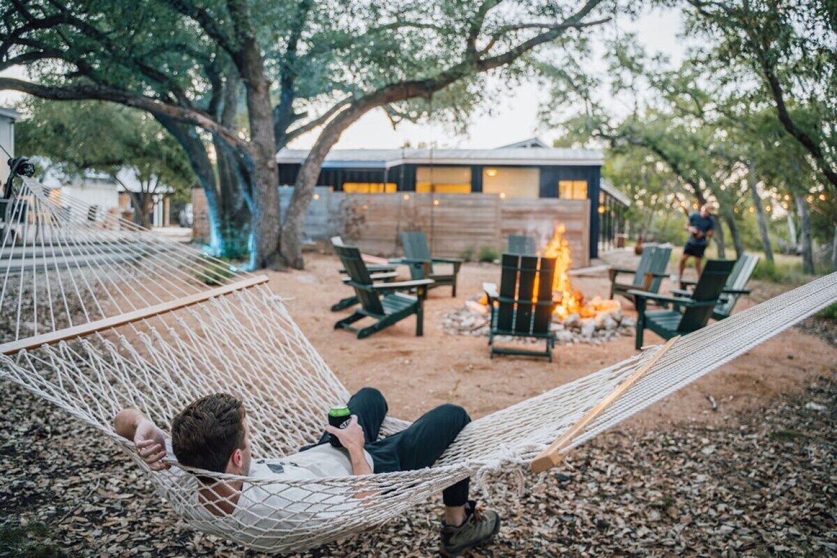 A hammock with a person reclining, a fire pit, and outdoor seating in a backyard setting.