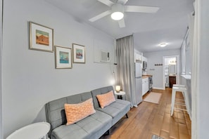 Ein modernes Wohnzimmer mit einem grauen Sofa, einem Deckenventilator und gerahmten Bildern an der Wand.