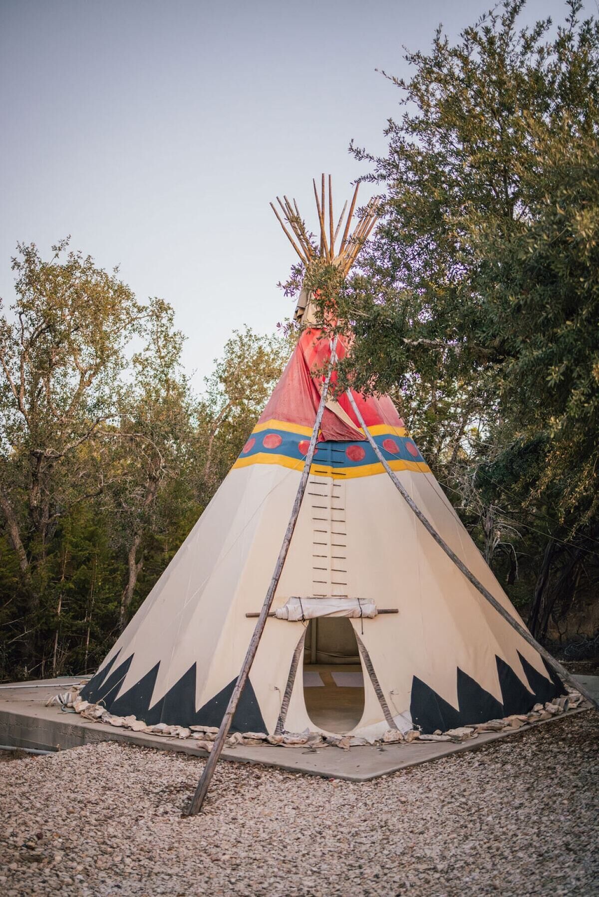 A tipi with a ladder leading to the entrance, surrounded by trees.