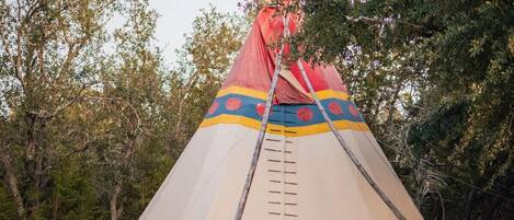 Un tipi con una escalera que lleva a la entrada, rodeado de árboles.