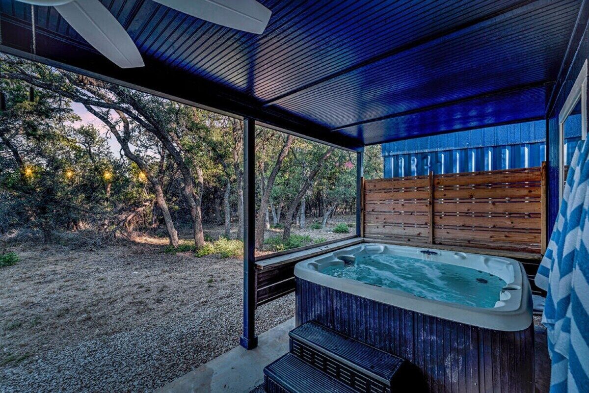 A hot tub in a covered outdoor area with a view of trees and a wooden fence.