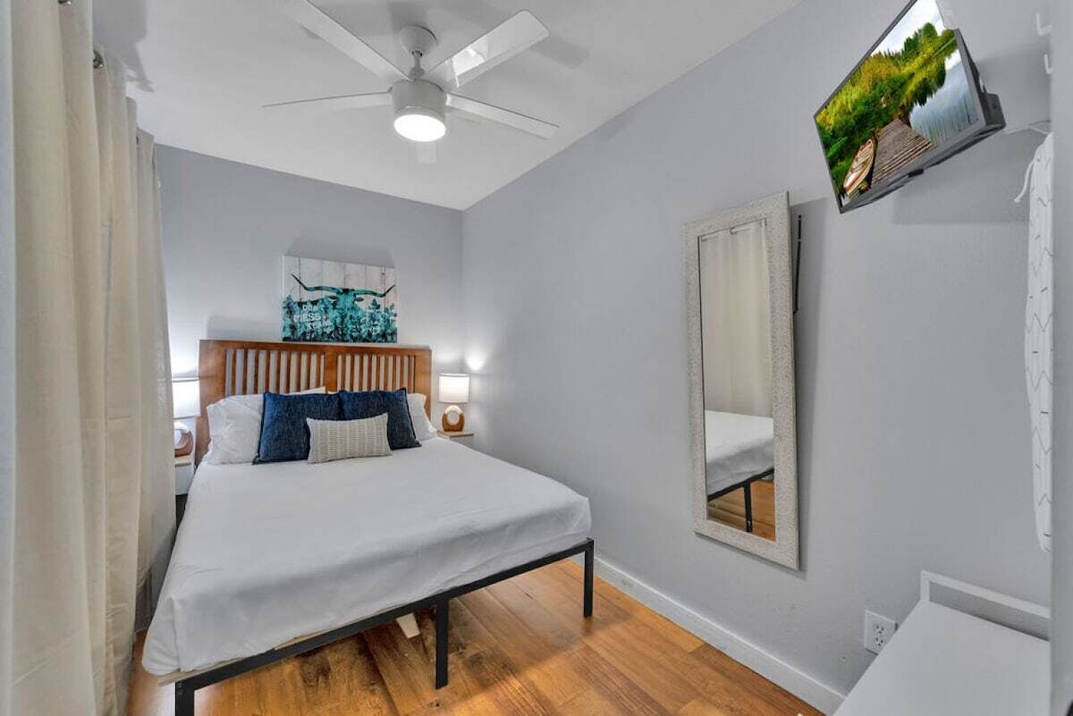 A bedroom with a bed, a ceiling fan, a mounted TV, and a large mirror.