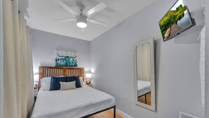 Une chambre à coucher avec un lit, un ventilateur de plafond, un téléviseur fixé au mur et un grand miroir.
