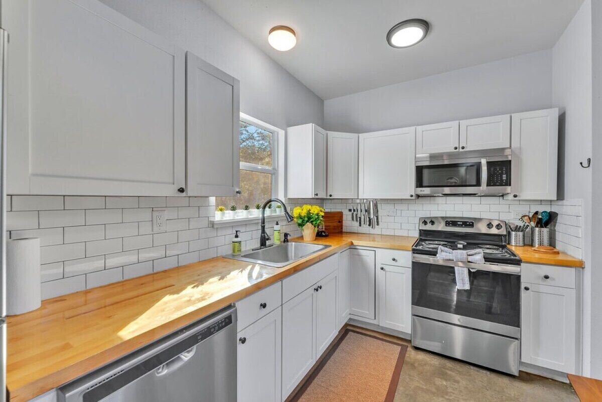 A modern kitchen with white cabinetry, a stainless steel microwave, an oven, and a dishwasher.