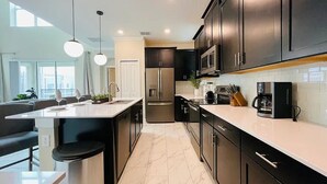A modern kitchen with dark cabinets, a large island, stainless steel appliances, and pendant lighting. - New 5BR/5BA home w/ private pool & hot tub, minutes to DIsney.  Sleeps up to 15. (Kissimmee)