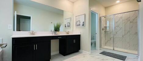 Un baño moderno con tocador doble, un espejo grande y una ducha a pie con azulejos de mármol.