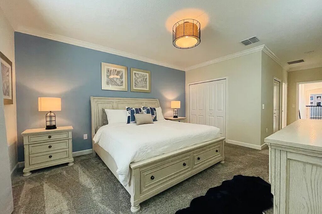 A bedroom with a bed, two bedside tables with lamps, a door, and a small rug.