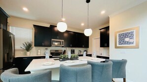 A modern kitchen with dark cabinets, a central island, and bar stools. - New 5BR/5BA home w/ private pool & hot tub, minutes to DIsney.  Sleeps up to 15. (Kissimmee)