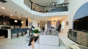 A spacious living area with a high ceiling, a dining area with a long table, and a seating area with a sofa and a TV. - New 5BR/5BA home w/ private pool & hot tub, minutes to DIsney.  Sleeps up to 15. (Kissimmee)