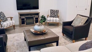 A living room with a flat-screen TV mounted on the wall, a fireplace, two armchairs, a sofa, and a coffee table with a decorative pumpkin centerpiece. - Spacious 4-bedroom townhome in charming American Fork with AC (American Fork)