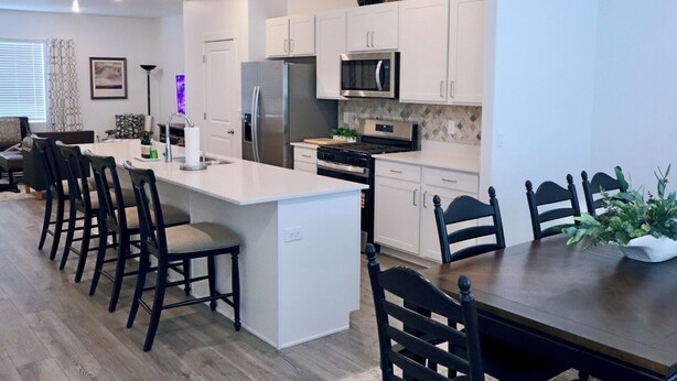 A modern kitchen with white cabinetry, a central island, and a dining area with black chairs. - Spacious 4-bedroom townhome in charming American Fork with AC (American Fork)