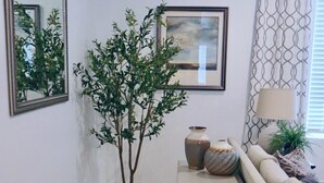 A living room with a wooden floor, a white side table with decorative items, a beige sofa, a mirror, and a framed painting. - Spacious 4-bedroom townhome in charming American Fork with AC (American Fork)