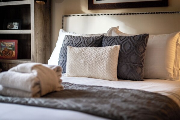 A neatly made bed with a quilted blanket, a pillow with a textured pattern, and a book titled 'Sleeping Bear' on a shelf.