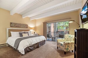 A bedroom with a bed, a chair, a TV, and a balcony with outdoor furniture.