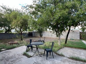 An outdoor patio with a round table and four chairs, surrounded by trees and a concrete wall. - Affordable Family Home Perfect for Monthly Stays! (Tucson)