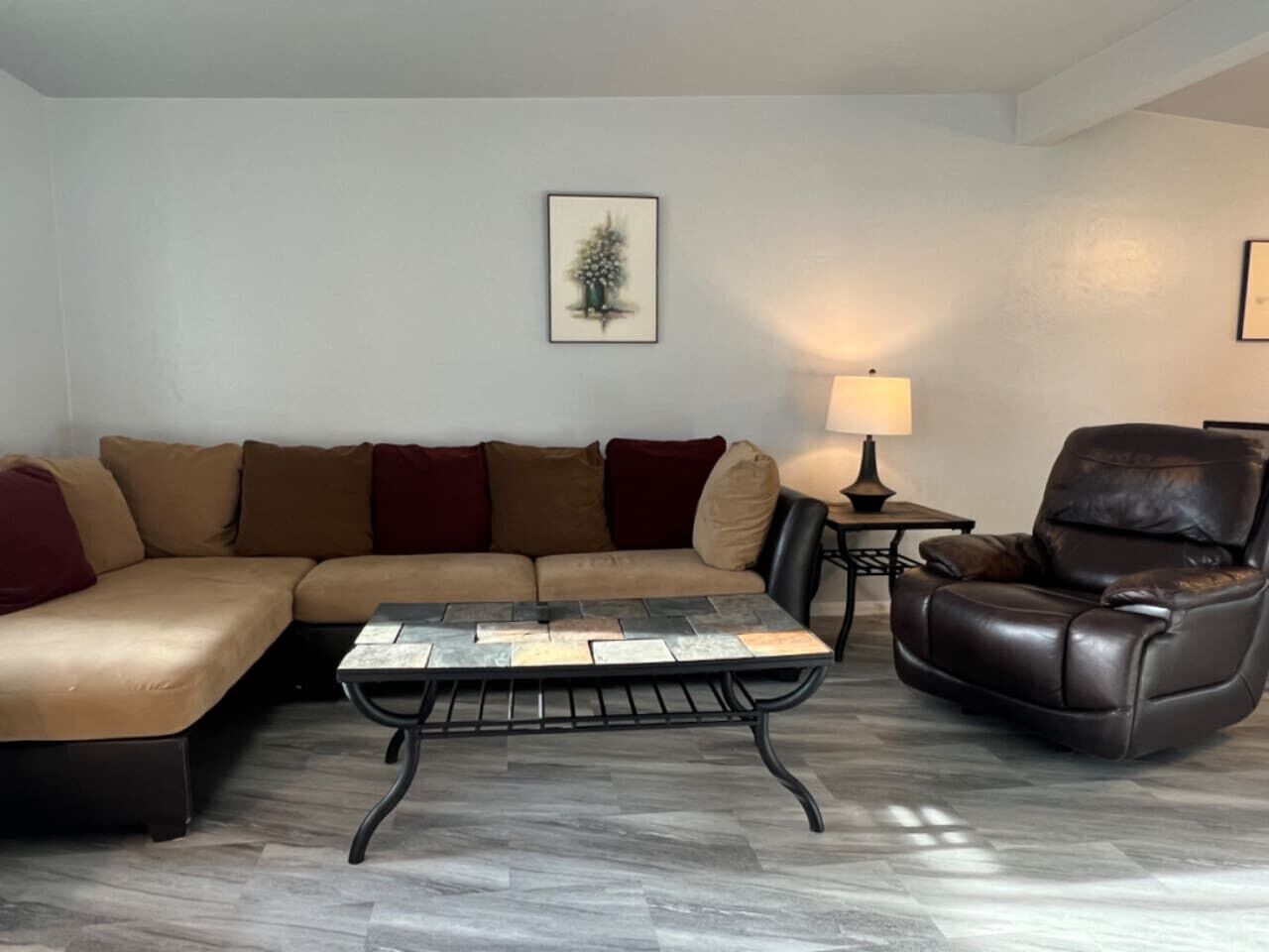 Ein Wohnzimmer mit einem Ecksofa, einem Couchtisch, einem Ledersessel und einer Lampe.