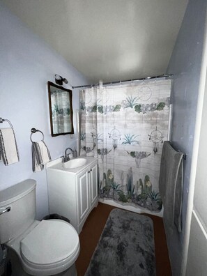 A bathroom with a toilet, sink, and shower curtain with a floral pattern. - Affordable Family Home Perfect for Monthly Stays! (Tucson)