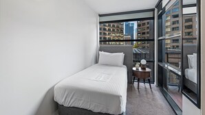 A small, modern bedroom with a bed, a small table, and a view of the city through large windows. - Chic Inner-city Stay With Balcony (Melbourne)
