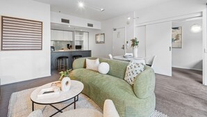 A modern living room with a green sofa, a coffee table, and a dining area with a white table and chairs. - Chic Inner-city Stay With Balcony (Melbourne)