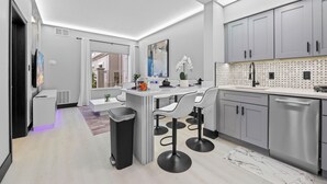 A modern kitchen with grey cabinets, a white countertop, and a black trash bin. - 1BR Apt, 2 Queens + Sofa, Near Disney (Orlando)