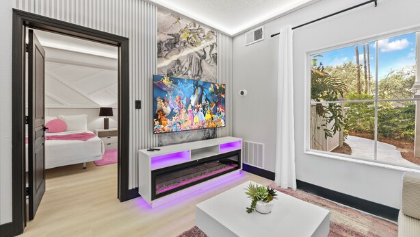 A modern living room with a large TV, a white sofa, and a view of the outdoors. - 1BR Apt, 2 Queens + Sofa, Near Disney (Orlando)