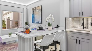 A modern kitchen with white cabinetry, a large window, and a dining area with a white table and chairs. - 1BR Apt, 2 Queens + Sofa, Near Disney (Orlando)