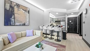 A modern living room with a sofa, a coffee table with a plant, and a painting on the wall. - 1BR Apt, 2 Queens + Sofa, Near Disney (Orlando)