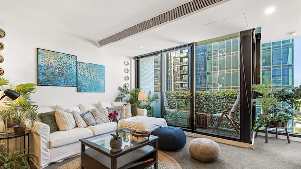 A modern living room with a white sofa, a glass coffee table, and a large sliding glass door leading to a balcony with plants. - Chic 2-bed Apartment With Balcony in Southbank (Melbourne)