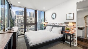 A modern bedroom with a large bed, a desk, and a view of the cityscape through floor-to-ceiling windows. - Chic 2-bed Apartment With Balcony in Southbank (Melbourne)