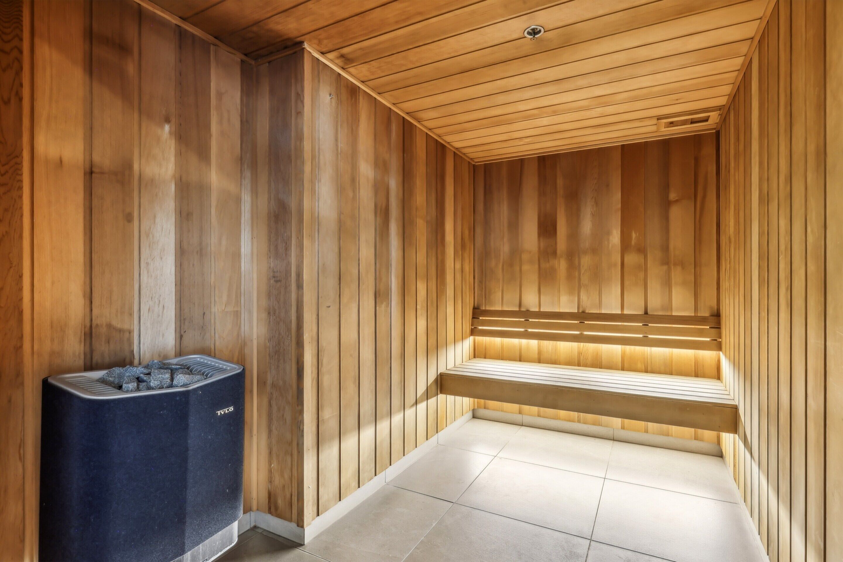 Una sauna con paredes y bancos de madera, piso de baldosas y un calentador de sauna.