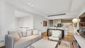 A modern living room with a grey sofa, a coffee table, and a dining area with a marble countertop. - Jewel Luxury Beachside 2-bed With Water View (Gold Coast)