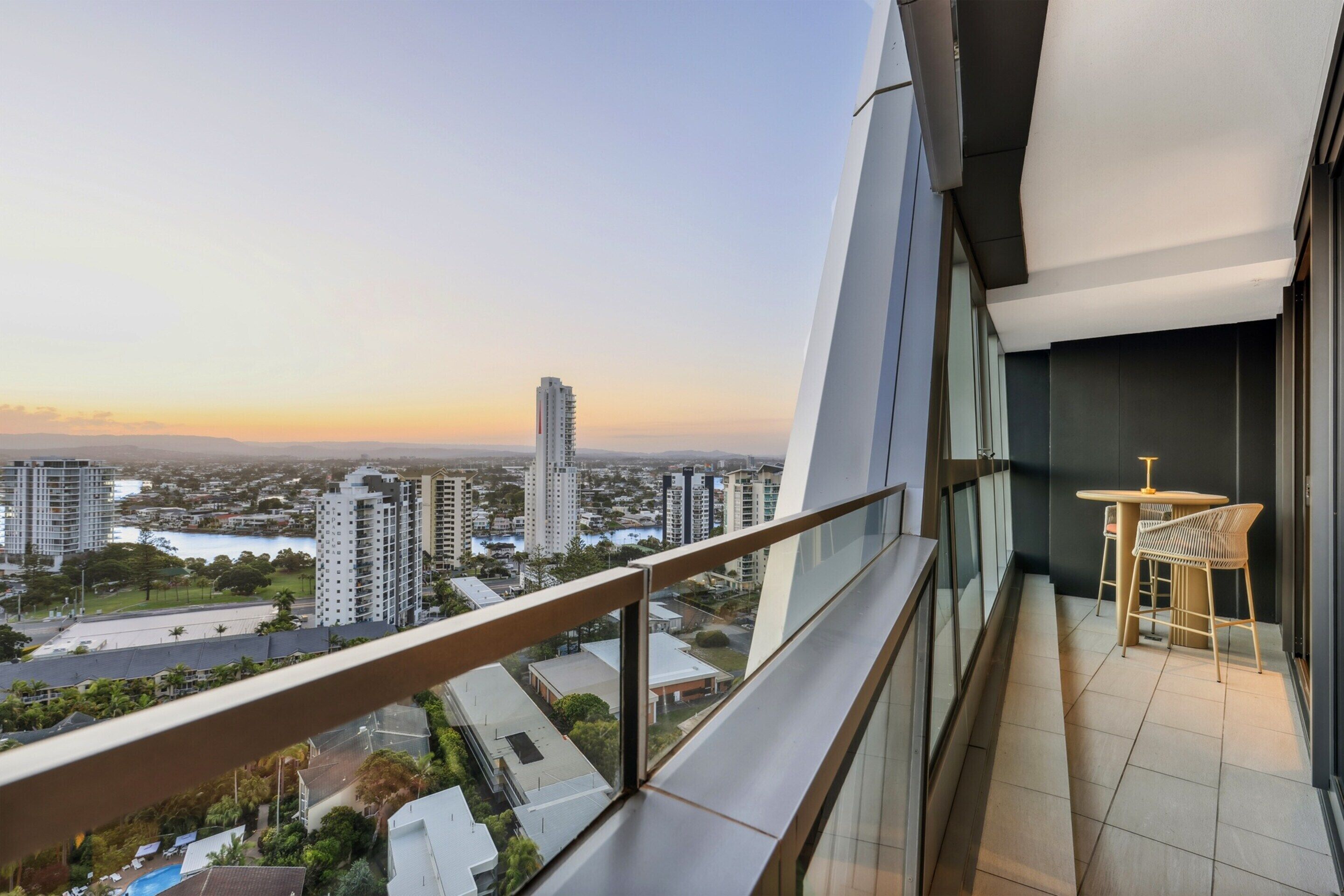 A balcony with a view of a cityscape, a table, and a chair.