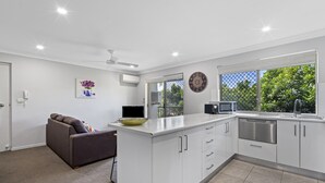 A modern kitchen with white cabinets, a built-in microwave, and a large window offering a view of greenery outside. - Charming 3-bed Apartment Near Local Shops (Brisbane)