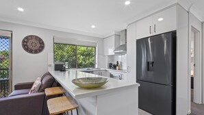 A modern kitchen with a large island, white cabinetry, and a black refrigerator. - Charming 3-bed Apartment Near Local Shops (Brisbane)