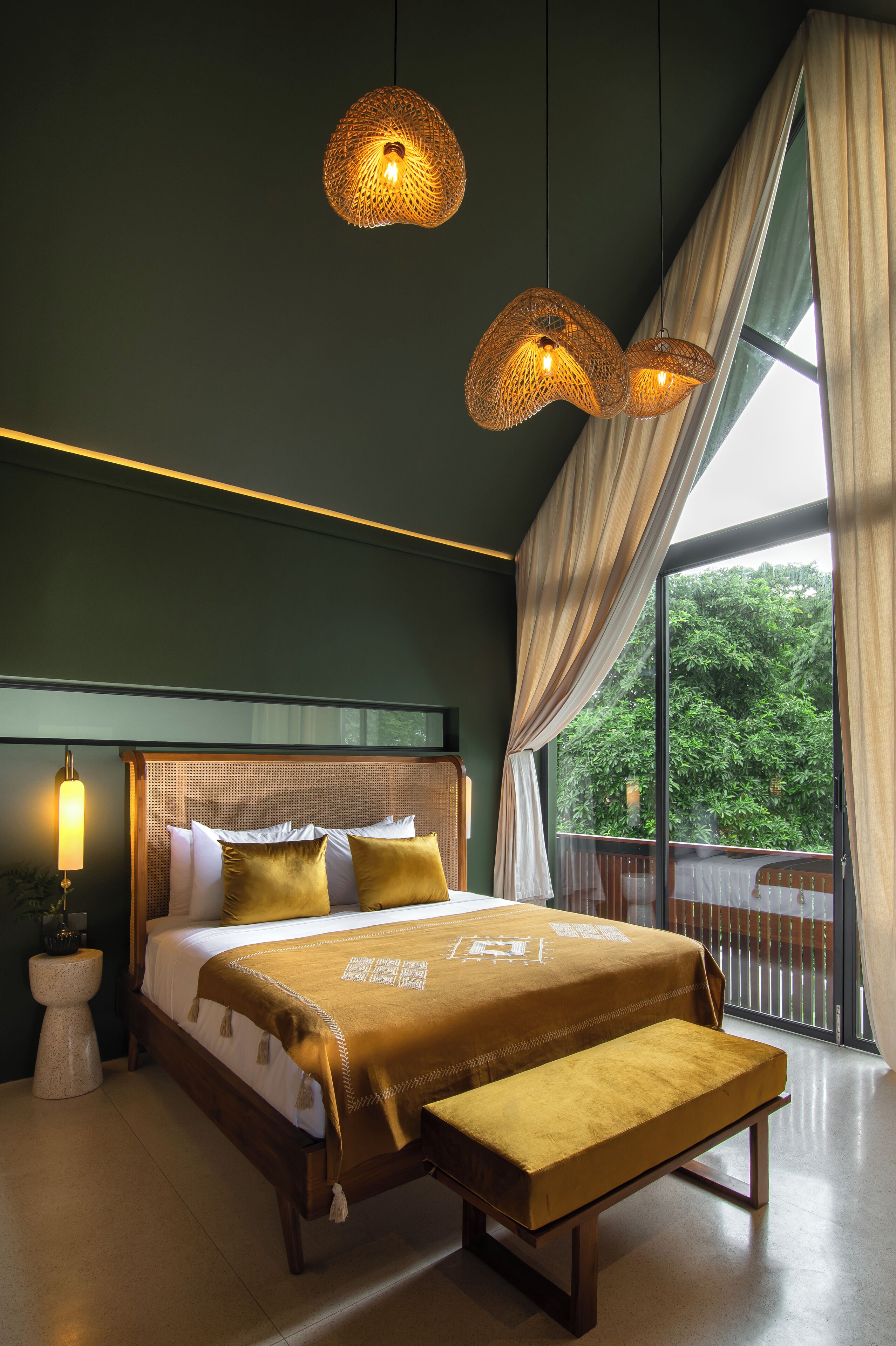 A bedroom with a large bed, a bench, and a view of greenery outside.