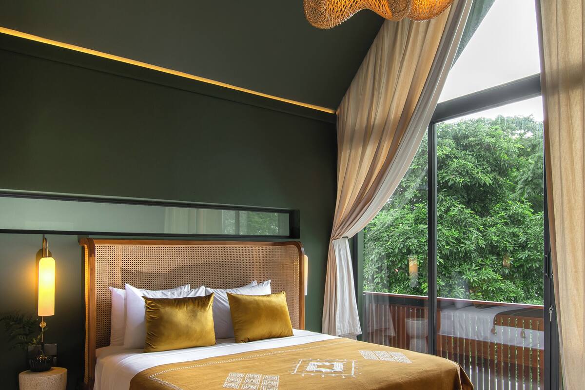 A bedroom with a large bed, a bench, and a view of greenery outside.