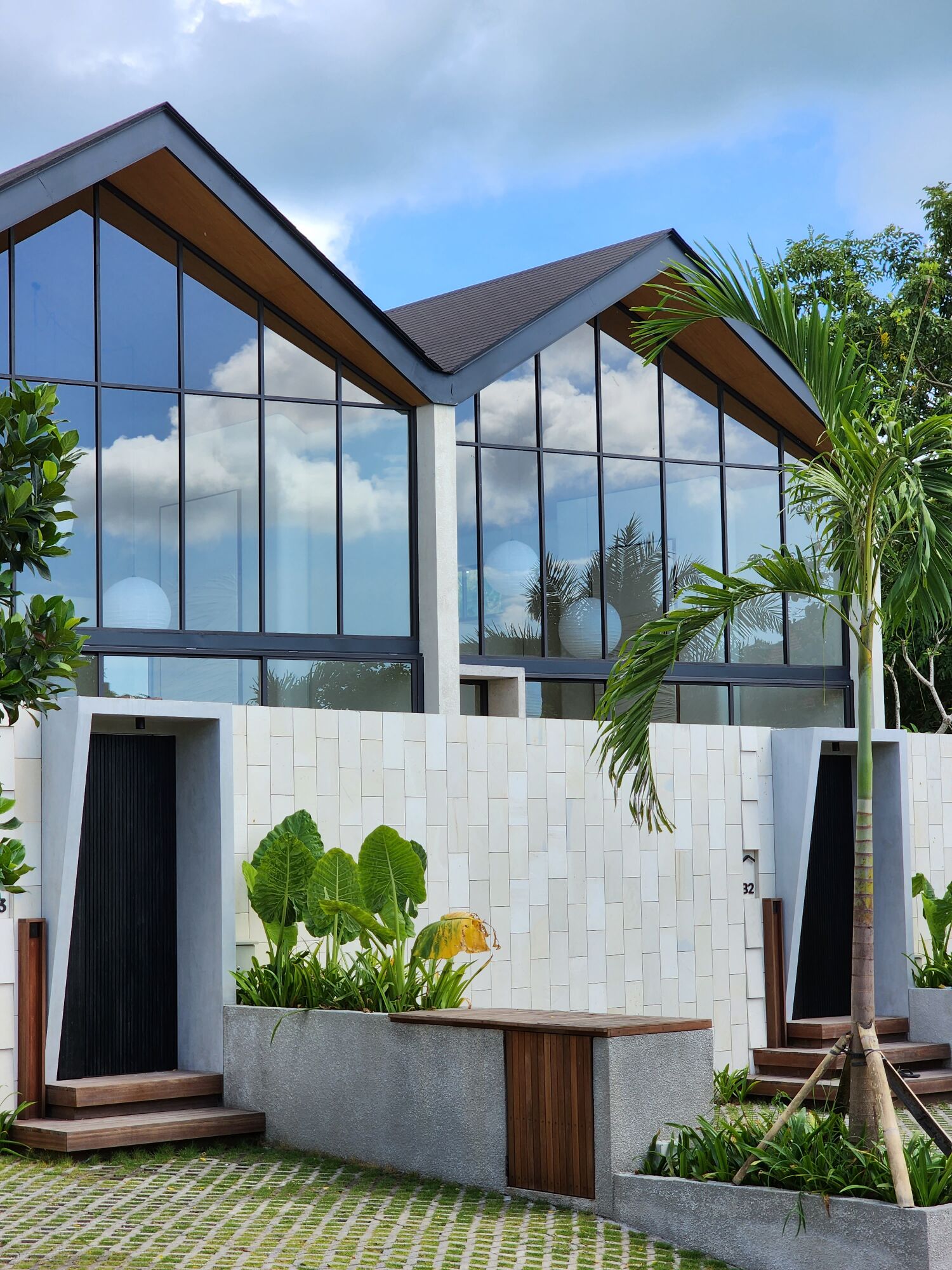 A modern house with large windows, a white exterior, and a garden with plants and a palm tree.