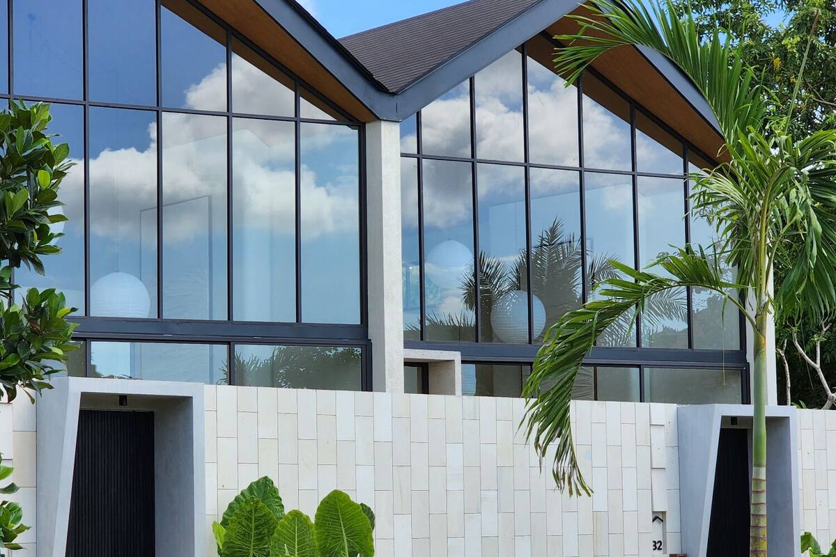 A modern house with large windows, a white exterior, and a garden with plants and a palm tree.