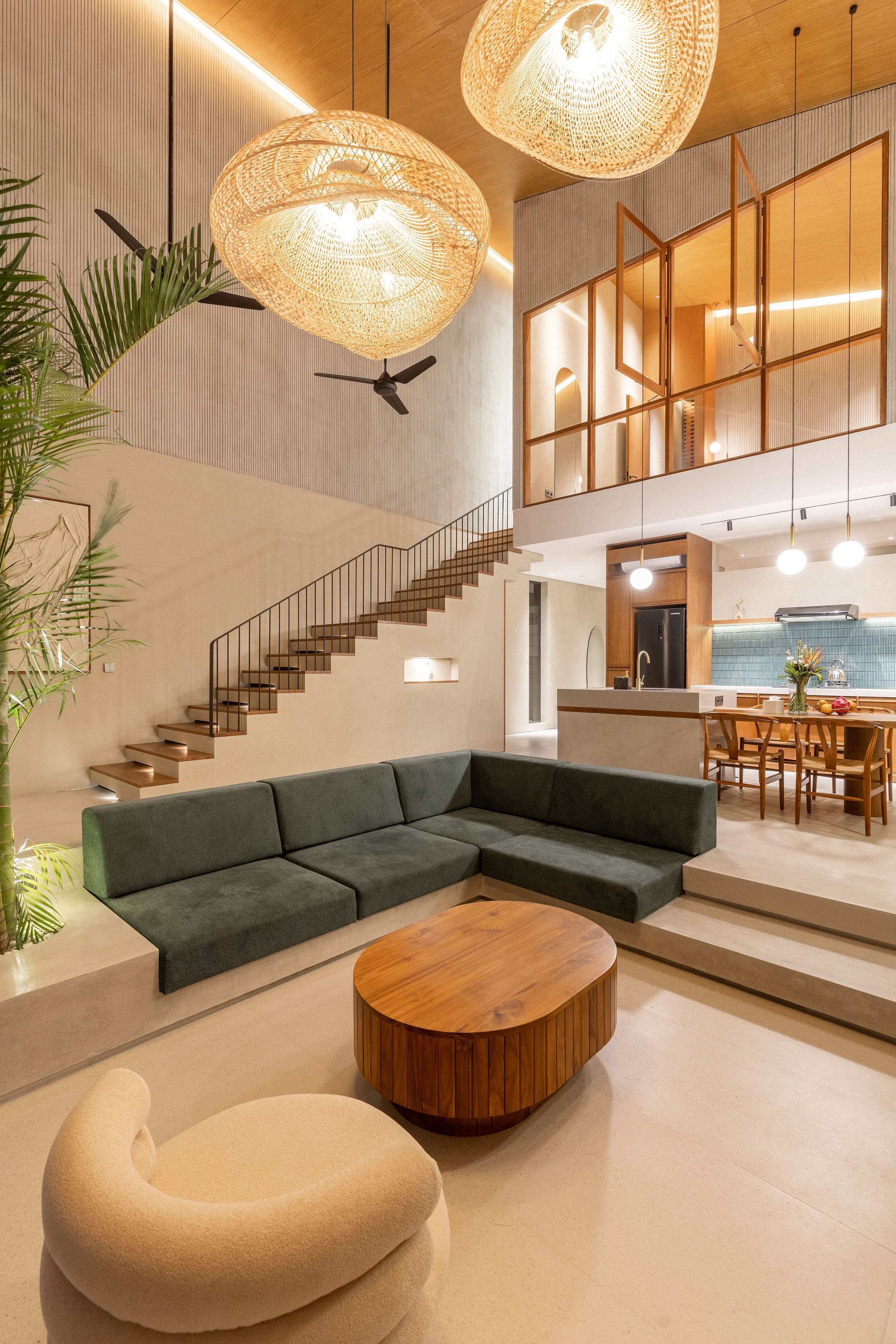 Un intérieur moderne avec un canapé d’angle, une table basse ronde en bois et un escalier menant à un niveau supérieur.