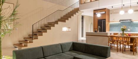 Un intérieur moderne avec un canapé d’angle, une table basse ronde en bois et un escalier menant à un niveau supérieur.