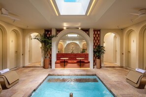 A swimming pool area with a central seating area, surrounded by arched doorways and potted plants.