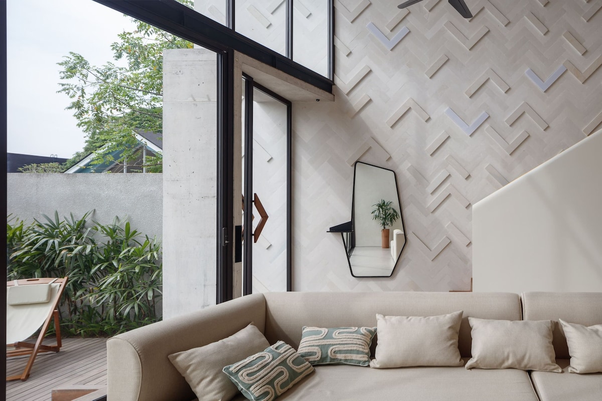 A modern living room with a beige sofa, a herringbone-patterned wall, and a large window.