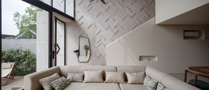 A modern living room with a beige sofa, a herringbone-patterned wall, and a large window.