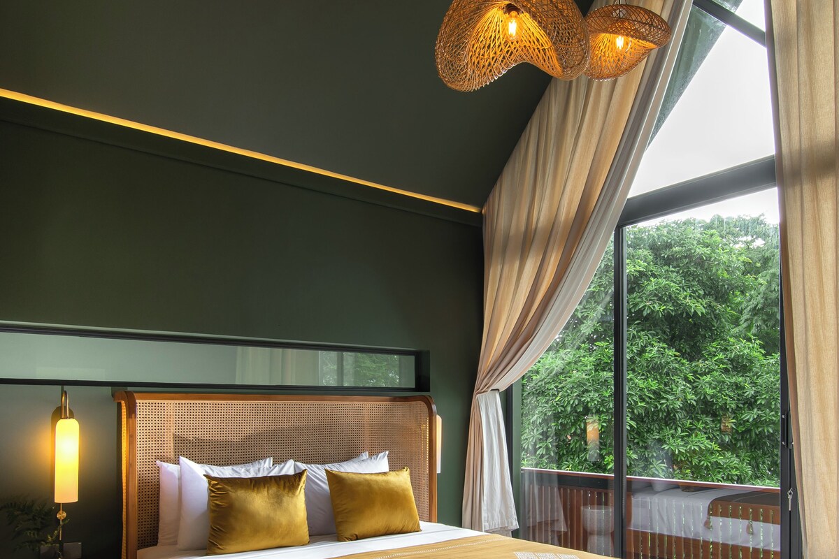 A bedroom with a large bed, a bench, and a view of greenery outside.