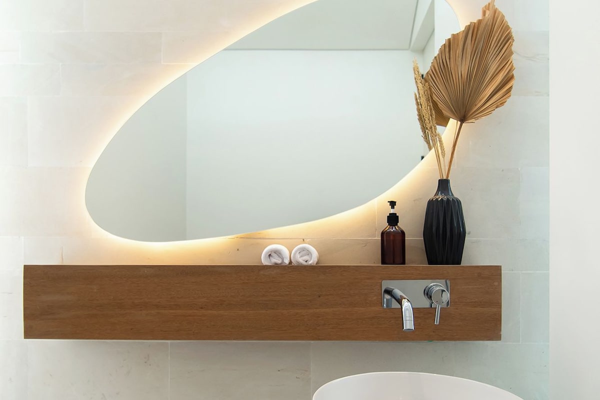 A modern bathroom with a large mirror, wooden shelf, and a round sink.