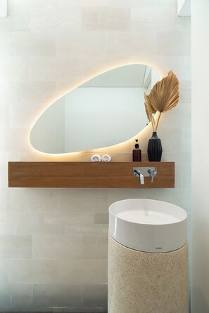A modern bathroom with a large mirror, wooden shelf, and a round sink.