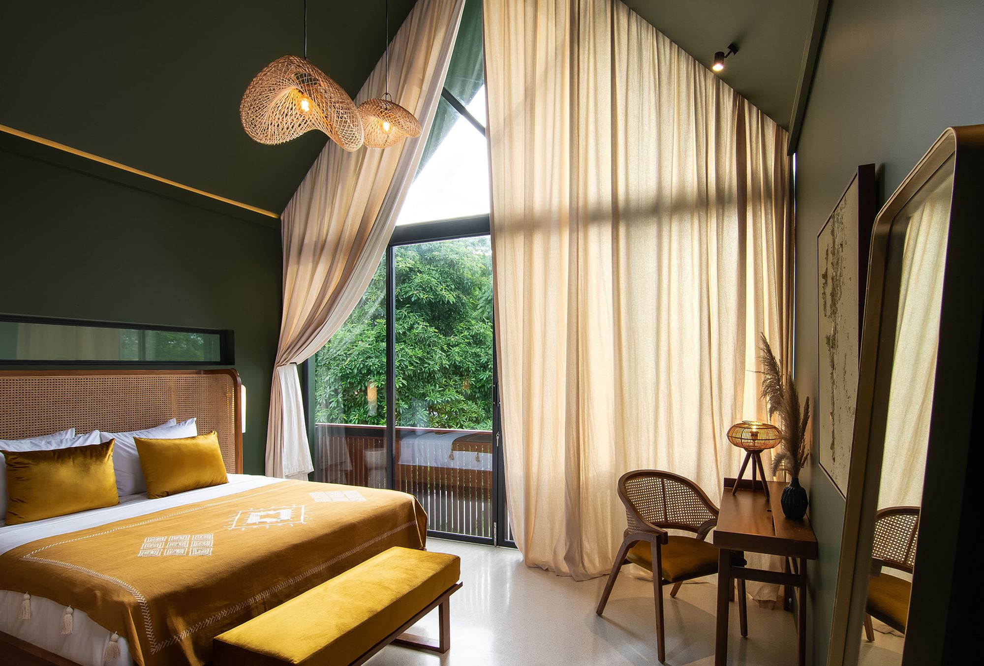 A modern hotel room with a large bed, a small desk, and a view of greenery outside.