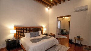 A bedroom with a wooden headboard, a bed with white bedding, two bedside tables with lamps, a small bedside table with a phone, a mirror, and a wooden floor. - Mirtala Hotel Boutique  (Guanajuato)